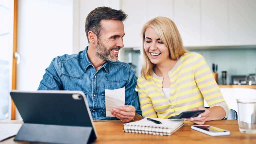 Happy couple talking about financing their house with some papers on the table and using a tablet