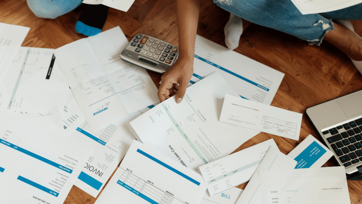 Persona organizando facturas y revisando cuentas con una calculadora y una laptop en el suelo, reflejando la importancia de la planificación financiera según la regla 50/30/20.