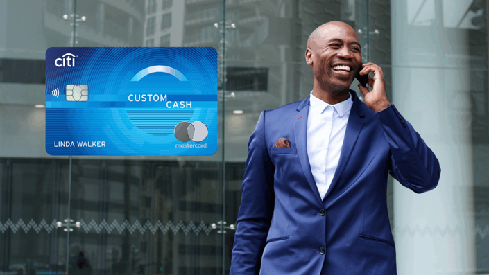Hombre elegante hablando por teléfono frente a un edificio de oficinas, con una tarjeta Citi Custom Cash Mastercard resaltada.