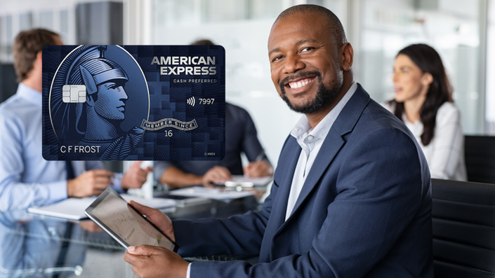 Hombre sonriente con una tarjeta American Express Blue Cash Preferred, usando una tablet mientras está en una reunión de negocios. Imagen relacionada con tarjetas de crédito American Express.