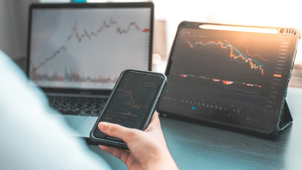 A person with a tablet, notebook and cell phone in hand investing in Stocks.