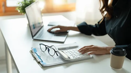 woman analyzing Smart Investment on her laptop and using a calculator, with a cup and her glasses beside her