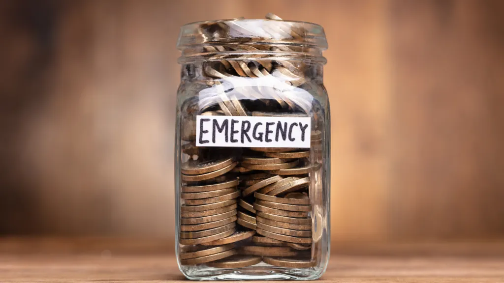 A jar labeled "Emergency Fund" filled with coins, representing the importance of saving to protect wealth.