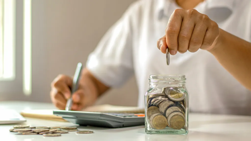 A person writing down their debts with a pen and paper and placing money in a safe