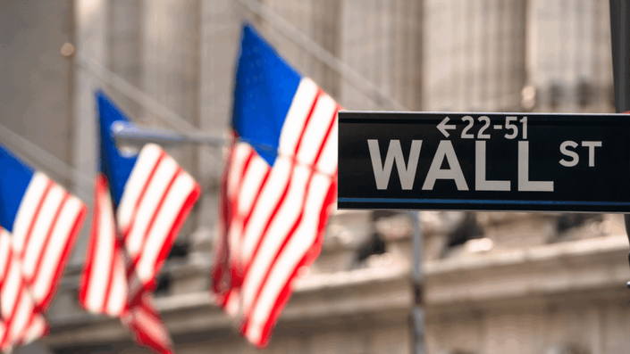 Cartel de Wall Street con varias banderas de Estados Unidos de fondo, representando el inicio en inversiones y el mundo de las acciones para principiantes en el mercado estadounidense.