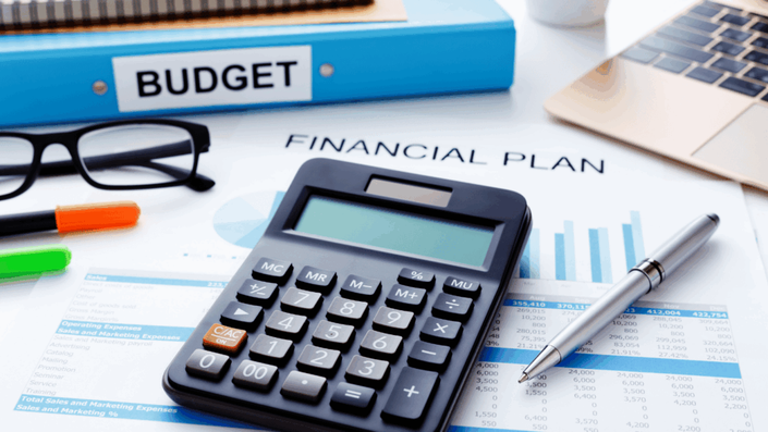 Desk with a calculator, financial plan documents, and a blue budget binder, representing financial planning for SA Inflation.
