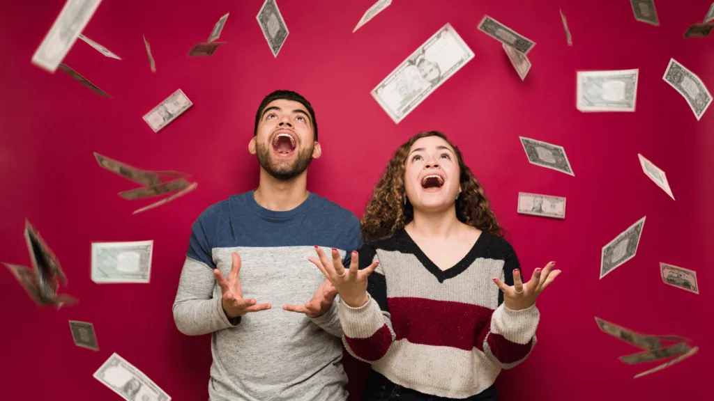 A happy couple celebrating as money falls around them, symbolizing achieving their financial goals and financial freedom.