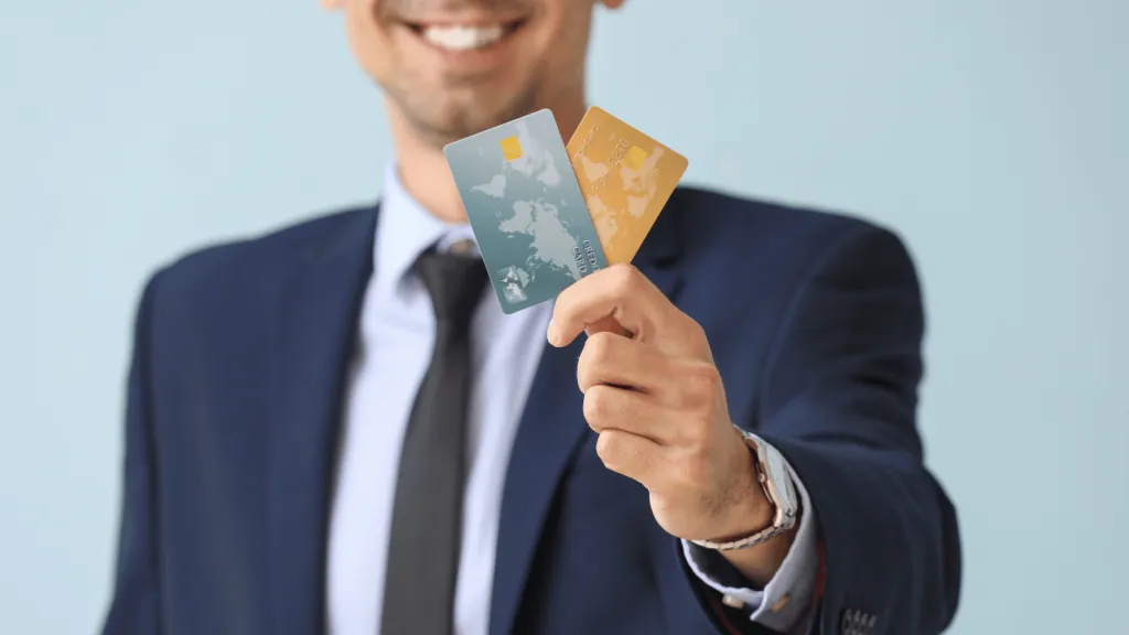 A businessman in a suit holding two credit cards with a smile, showcasing different card options. He appears to be presenting the best credit card choices for financial management.