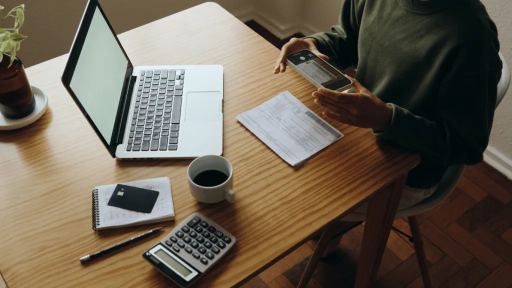 A person paying their debts and managing finances due to credit card expenses, with bills, a calculator, and a laptop on the desk.