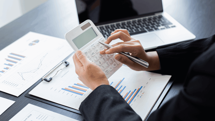 Primer plano de unas manos usando una calculadora sobre gráficos, en un acto de planificación y organización de las finanzas personales durante un divorcio.