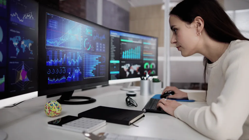 Financial analyst using technology to track the impact of technological advancements – A professional monitoring financial market trends on multiple screens, highlighting the role of technology in investment strategies.