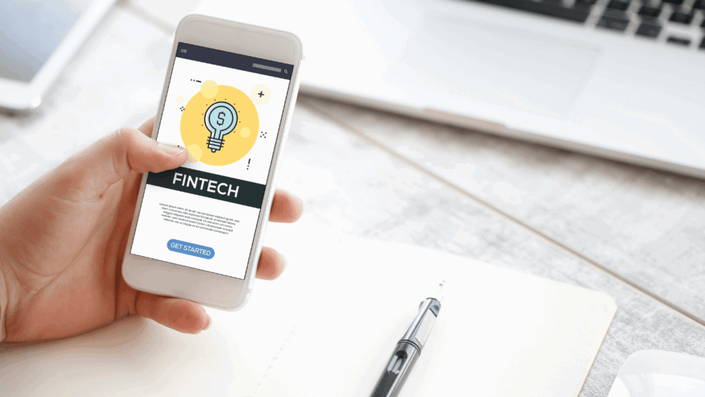 A person using a smartphone displaying the word "Fintech" on a digital screen, representing the rise of fintech solutions in modern finance.