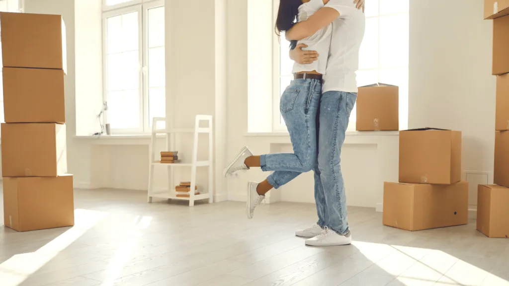 Happy couple in their new home surrounded by moving boxes, celebrating their decision on buying vs. renting their dream property.