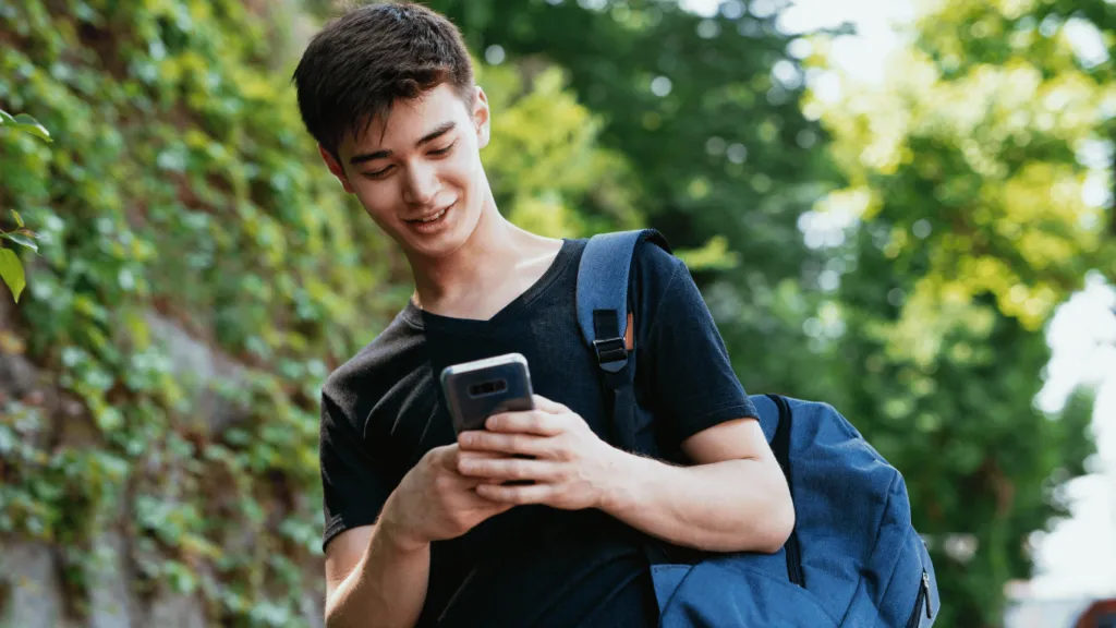 A smiling young man using his smartphone to check Apps to Manage Finances, tracking expenses and managing his budget on the go.