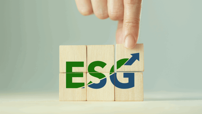 Mano colocando un bloque de madera con una flecha hacia arriba sobre las letras "ESG" en bloques, simbolizando el crecimiento en la inversión de impacto con un enfoque en sostenibilidad y gobernanza.