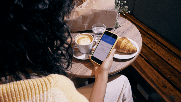 A woman using a mobile banking app in a café, showcasing the convenience of fintech for managing personal finances in South Africa.