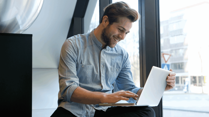 Hombre sonriendo con satisfacción al ver en su laptop los resultados positivos de una buena gestión de sus finanzas personales y su nuevo comienzo.