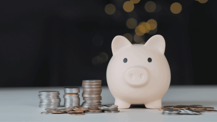 Light pink piggy bank surrounded by stacks of coins on a white table, symbolizing saving money during SA Inflation.