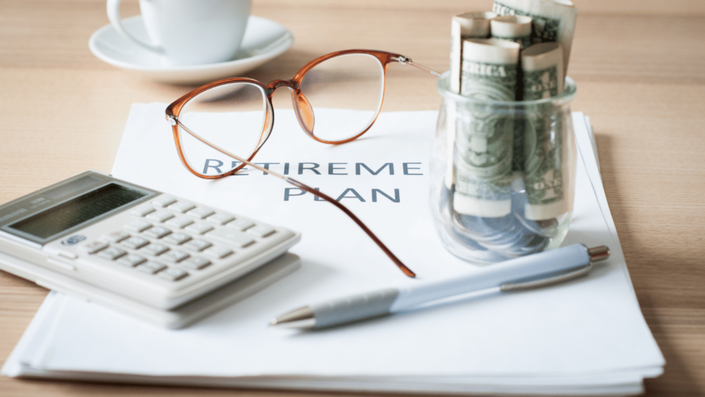 A Two-Pot Retirement System plan document with glasses, calculator, and rolled money, symbolizing careful planning for retirement.