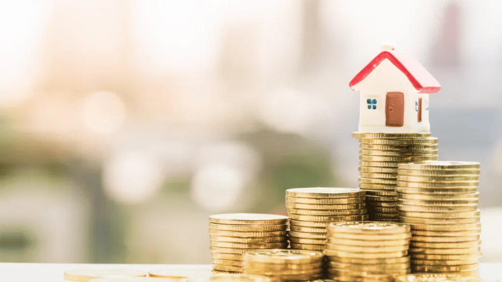 A miniature house placed on top of stacked gold coins, representing financial growth and returns from investing in real estate.