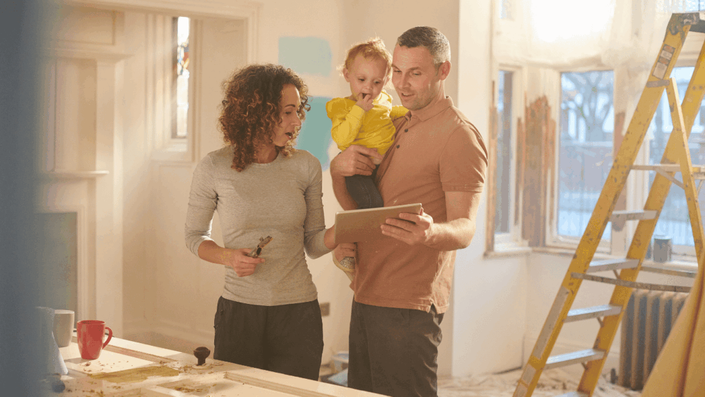 Familia planificando una reforma en casa, revisando un tablet en una habitación en obras con escalera y herramientas, mientras aprenden a presupuestar reformas del hogar de manera efectiva.