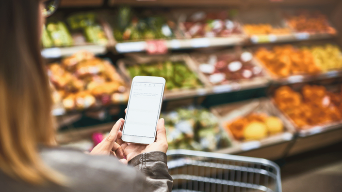 A shopper checking a grocery list in a supermarket, showcasing a practical way to save money on a tight budget by planning meals and shopping smartly.
