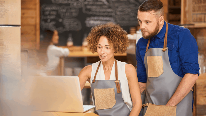 Two small business owners in a cafe setting up a new Tap-to-pay payment terminal, looking at a laptop together.