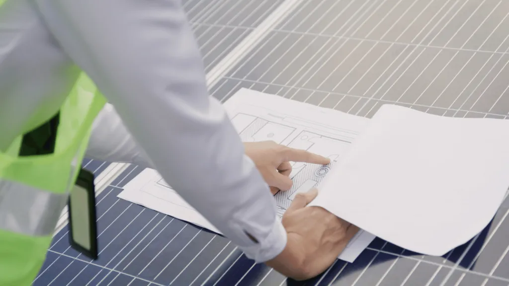 An engineer analyzing blueprints on a large solar panel installation, representing the growth of Renewable Energy Investments in South Africa.