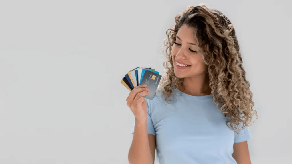 Mujer de cabello rizado y camiseta azul sonriendo mientras sostiene varias tarjetas de crédito sin un SSN. Logró obtenerlas sin necesidad de un número de Seguro Social, demostrando que es posible acceder a crédito en EE. UU. sin este requisito.